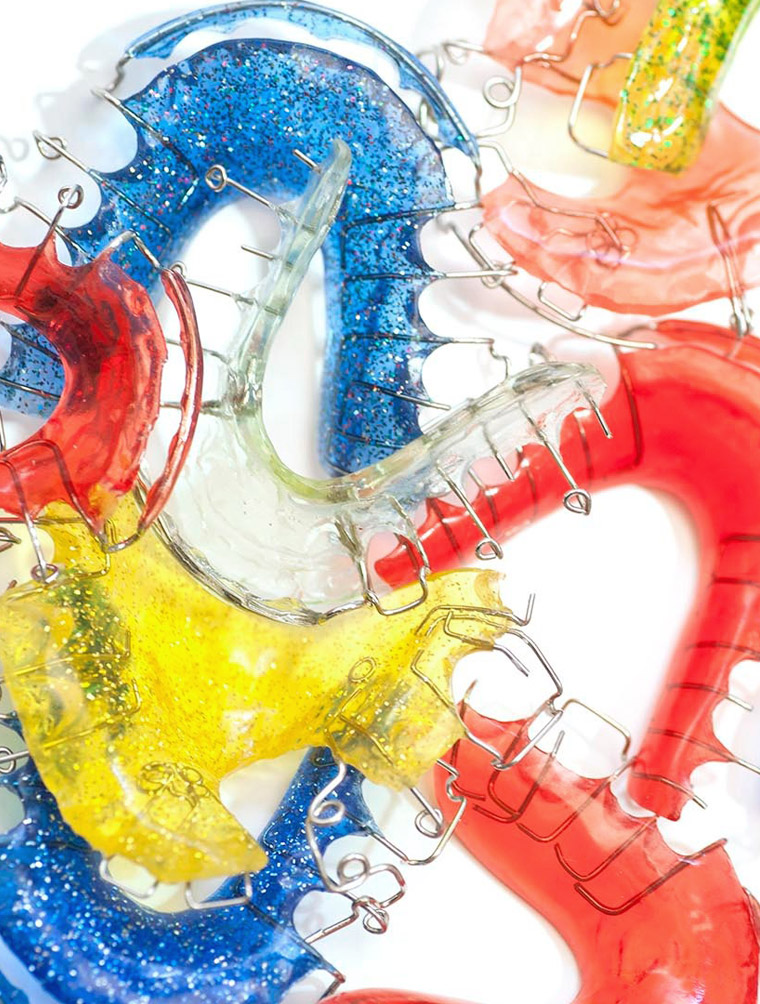 Colorful dental models and orthodontic appliances displaying blue, red, and yellow dental equipment on white surface.