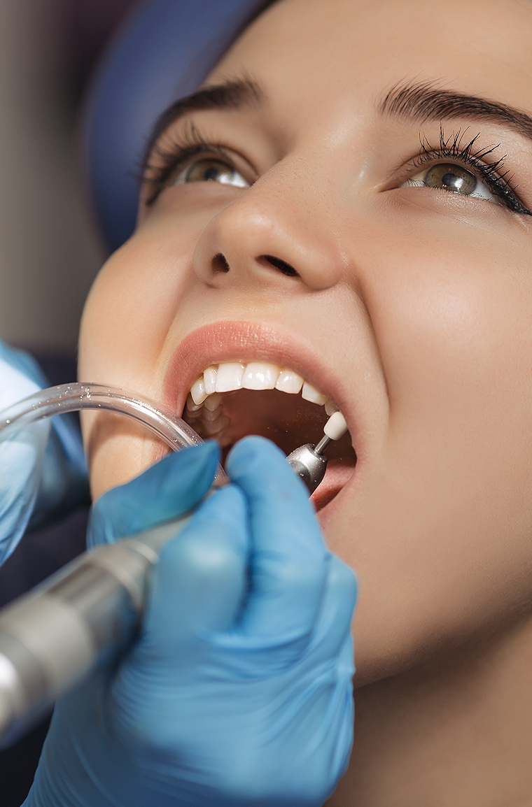 Dentist in blue gloves examining patient's teeth during dental procedure.