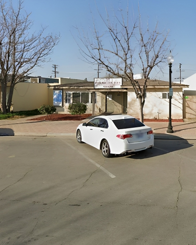White car parked in front of dental office building with bare trees and clear sky.