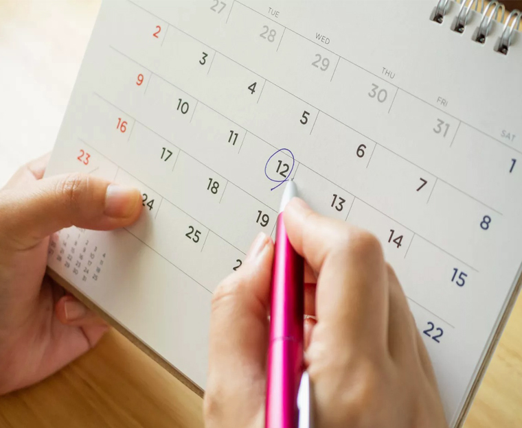 Hand marking calendar date with red pen on dental office desk.
