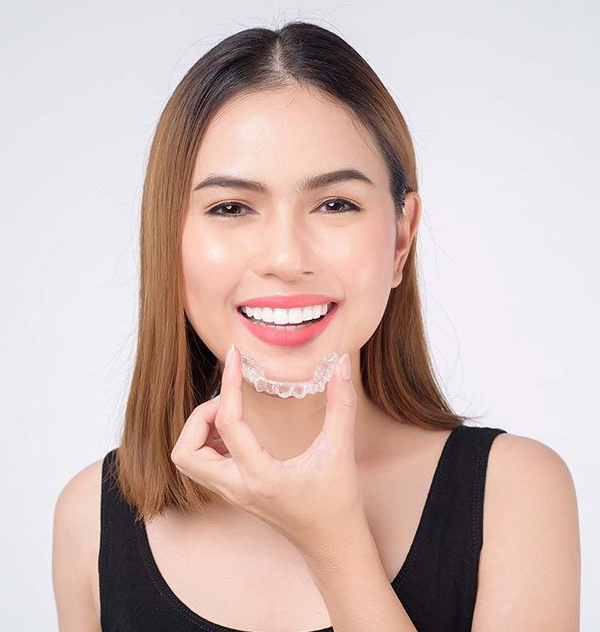Woman holding dental aligner, smiling at camera against white background, orthodontic treatment display.