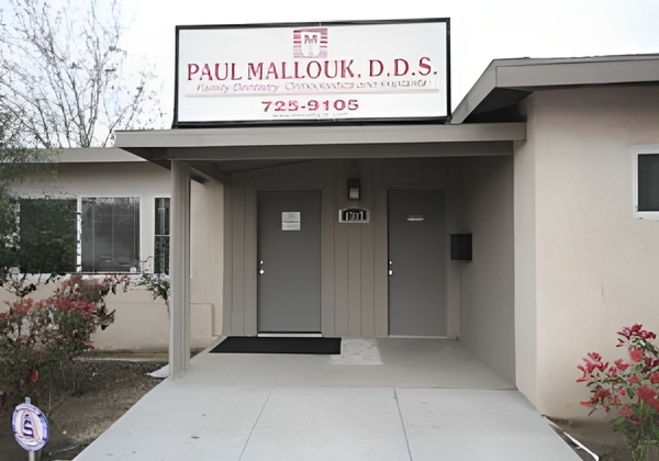 Dental office exterior with sign reading "Paul Mallouk, D.D.S." and phone number on storefront.