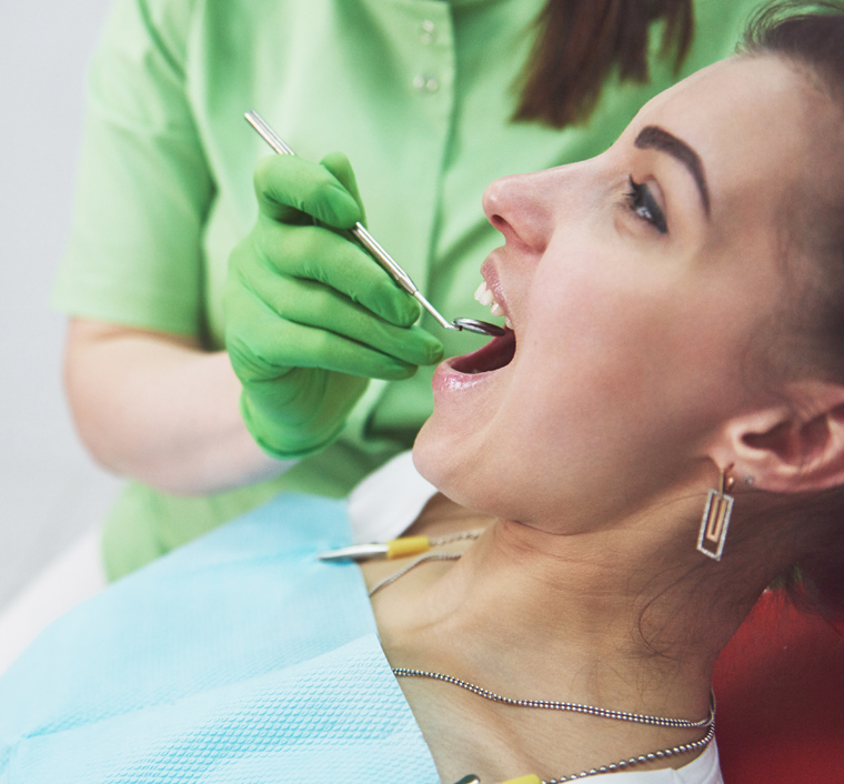Dentist in green gloves examining patient's teeth during dental procedure in clinical setting.
