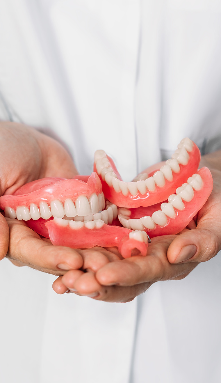 Dentist holding red dentures in hands against white coat background.