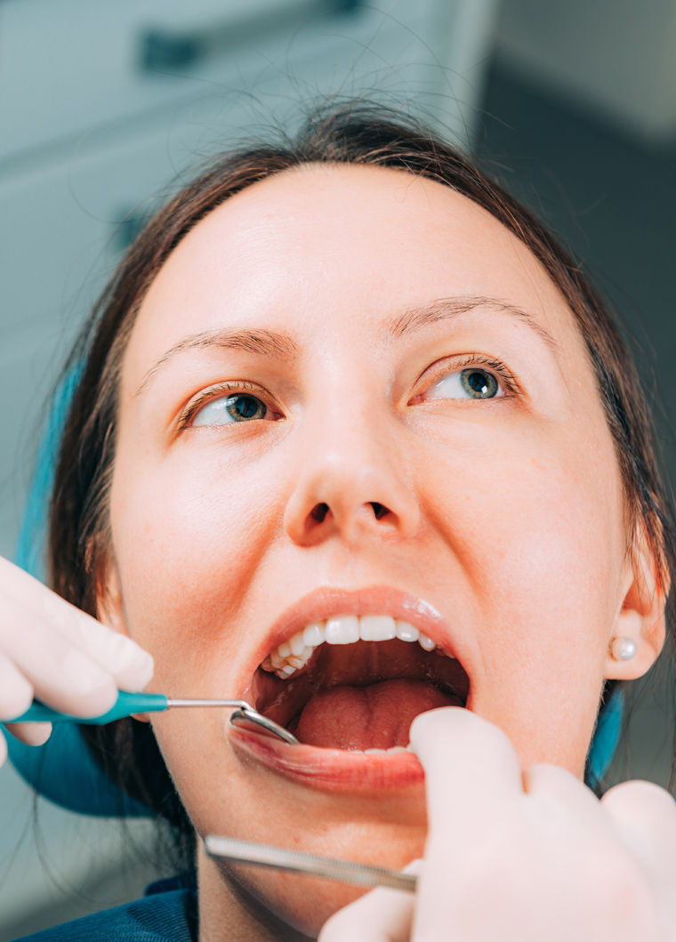 Woman receiving dental examination with mirror and tool in dentist's office.