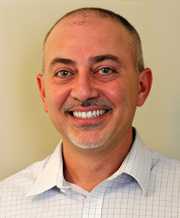 Professional headshot of Paul Mallouk, D.D.S., smiling in light blue button-up shirt against neutral background.