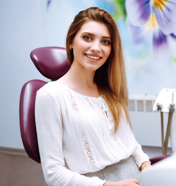 Woman in white top seated in dental chair, smiling at camera in modern dental office.