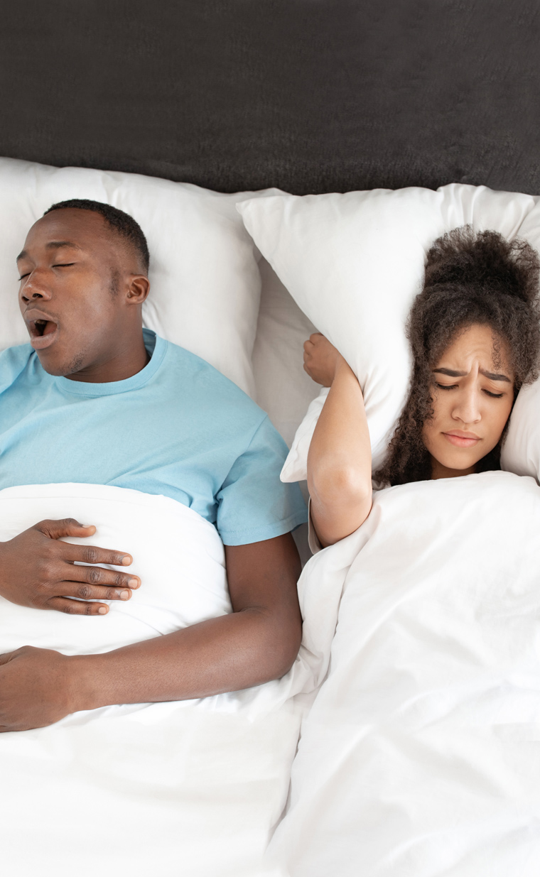 Couple in bed showing sleep disturbance; man awake while woman sleeps, illustrating sleep issues.